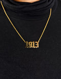 Gold necklace with '1913' pendant on a black background