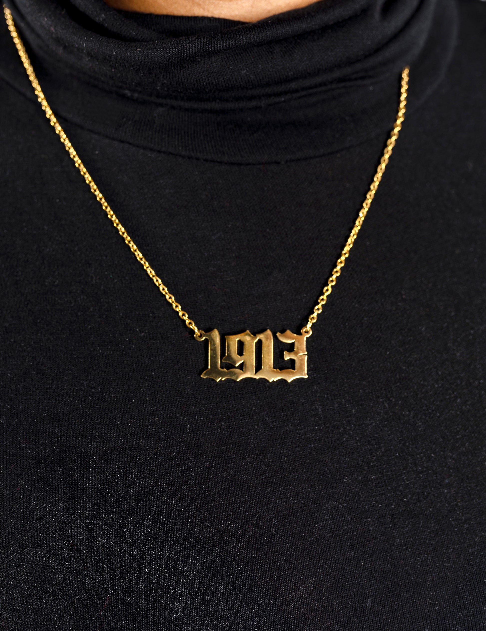 Gold necklace with '1913' pendant on a black background