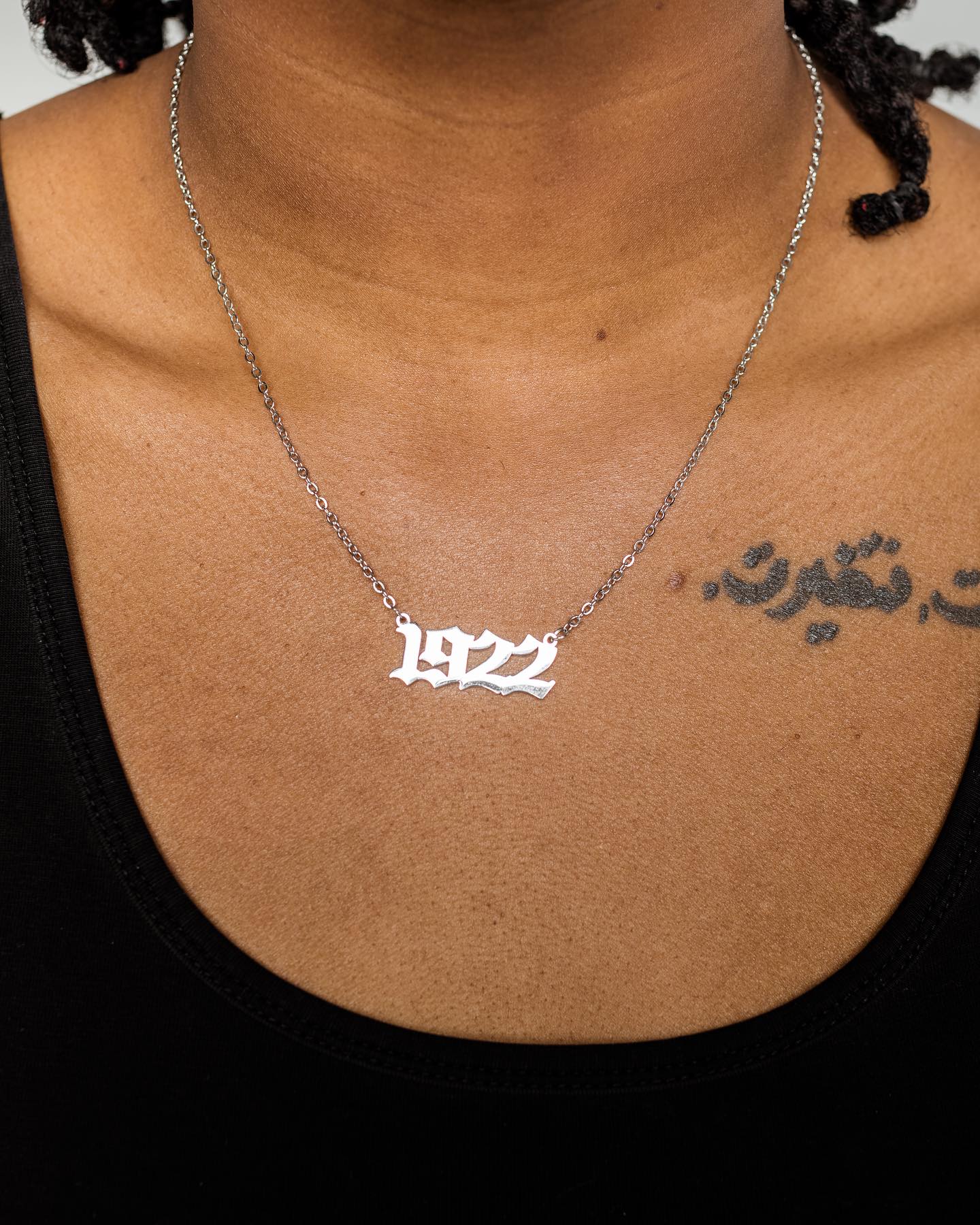 Silver '1972' necklace on a person's neck with a black background