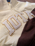 Close-up of a beige hoodie with 'IOTA' branding on a wooden surface