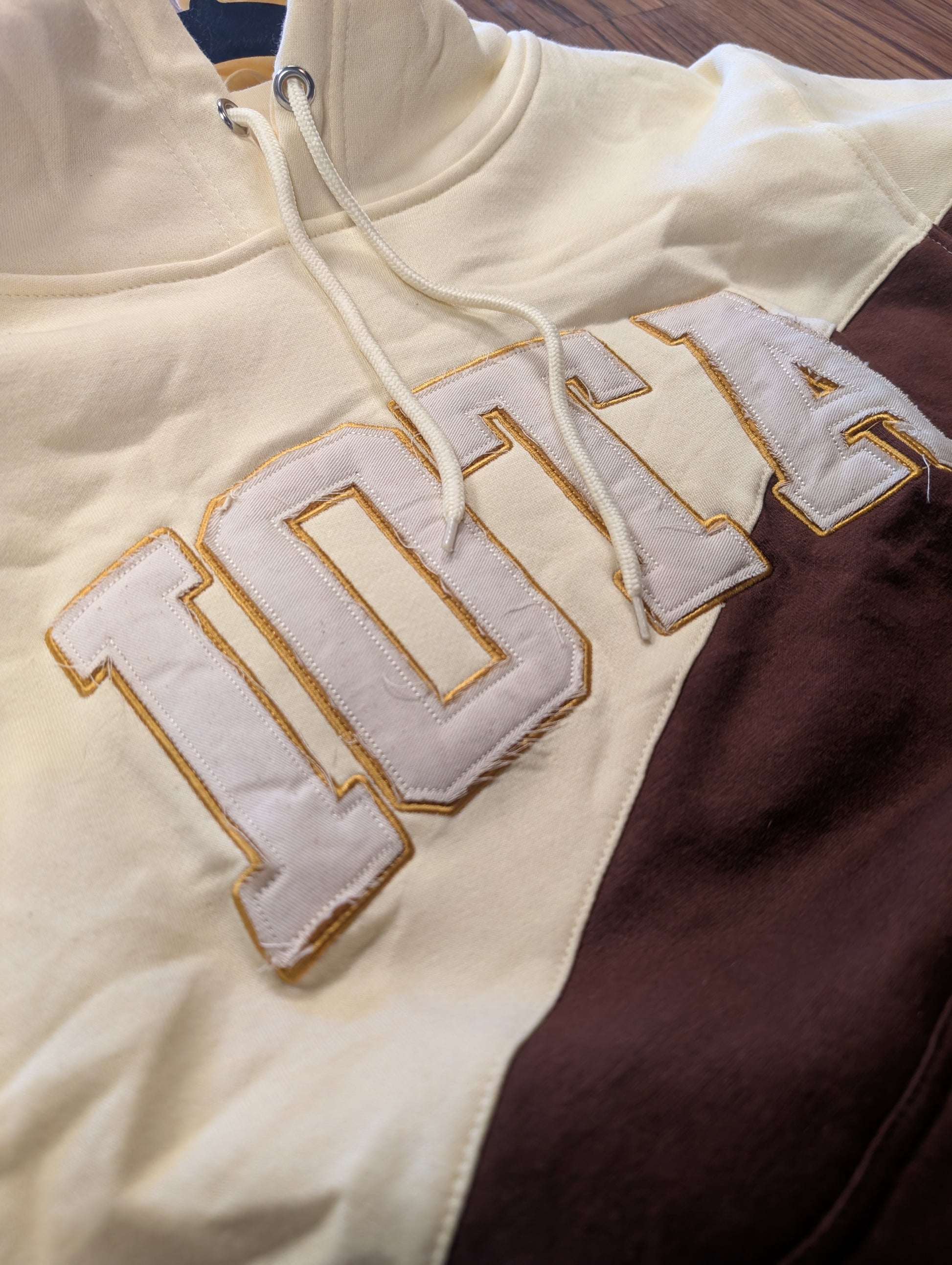 Close-up of a beige hoodie with 'IOTA' branding on a wooden surface