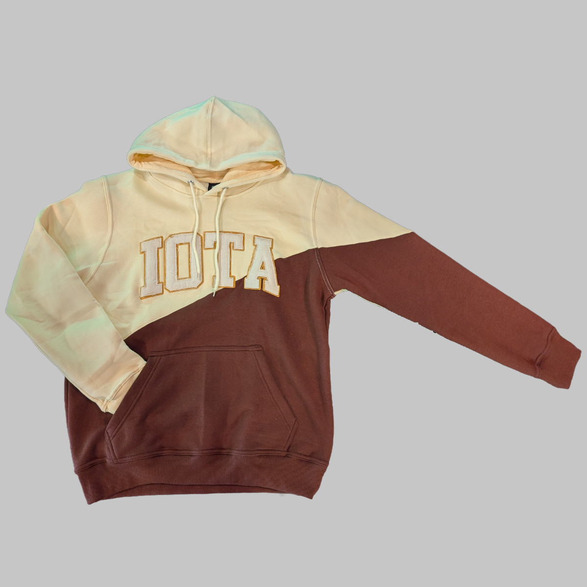 Two-tone hoodie with beige top and brown bottom on a gray background. Iota written across the front in distressed letters