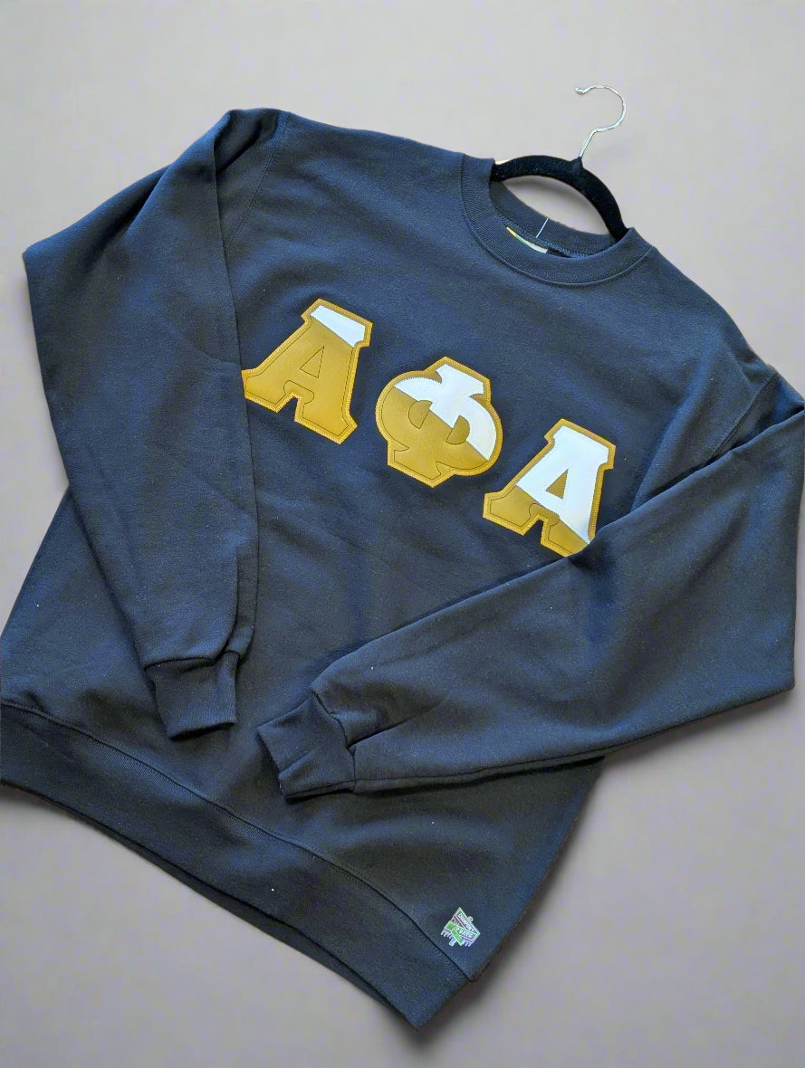 Person wearing a black sweatshirt with gold letters, holding a backpack outdoors.