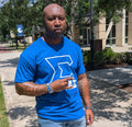 Man wearing a blue t-shirt with a White Sigma and GOMAB written underneath, standing outdoors on a sidewalk.