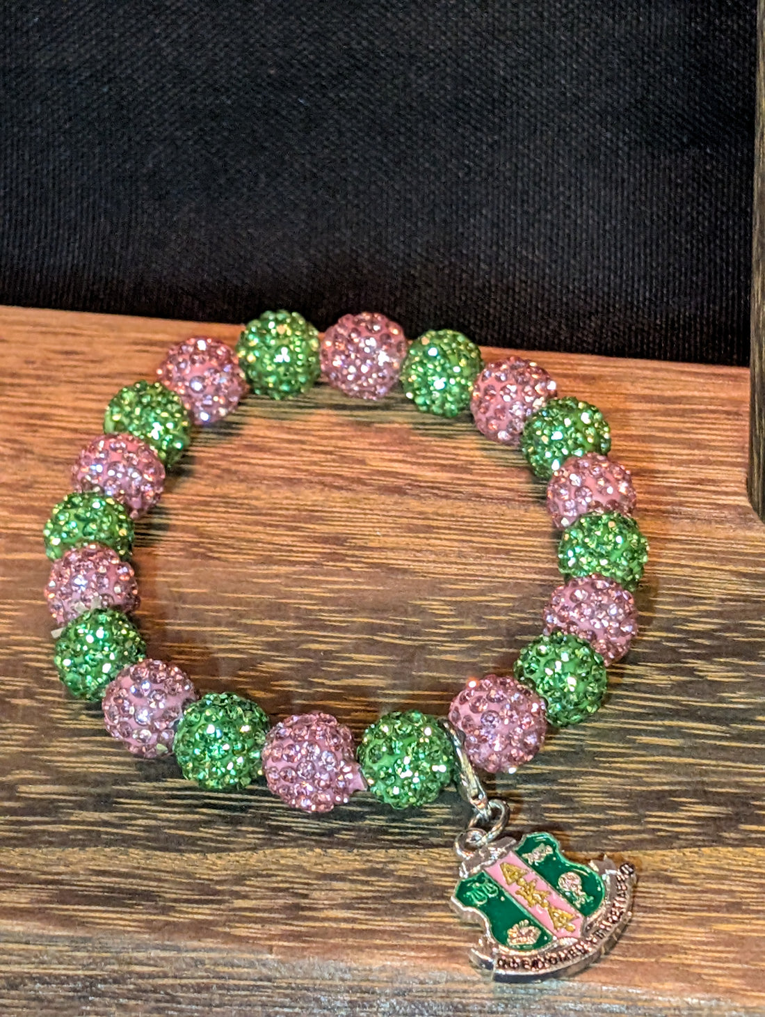 Bracelet with pink and green beads and a silver charm on a black background