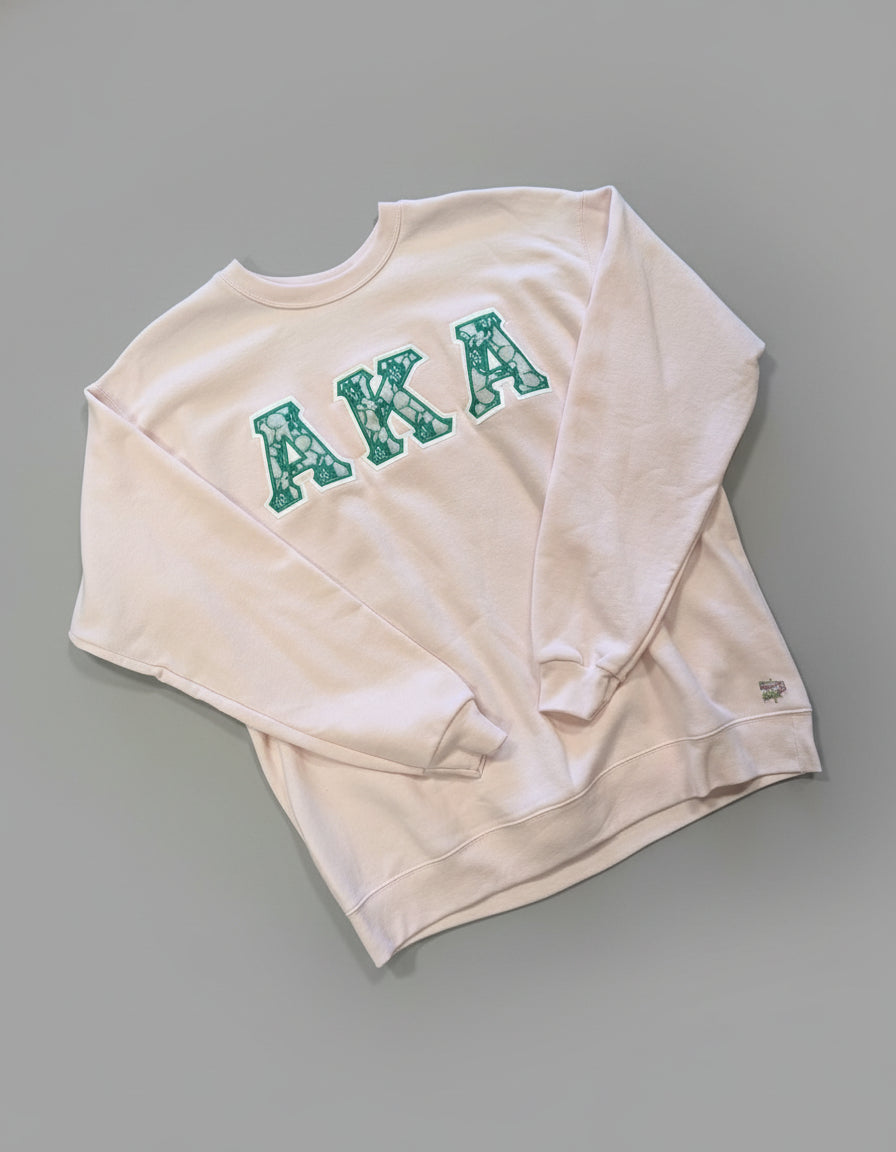 Light pink sweatshirt with 'AKA' in green letters on a gray background