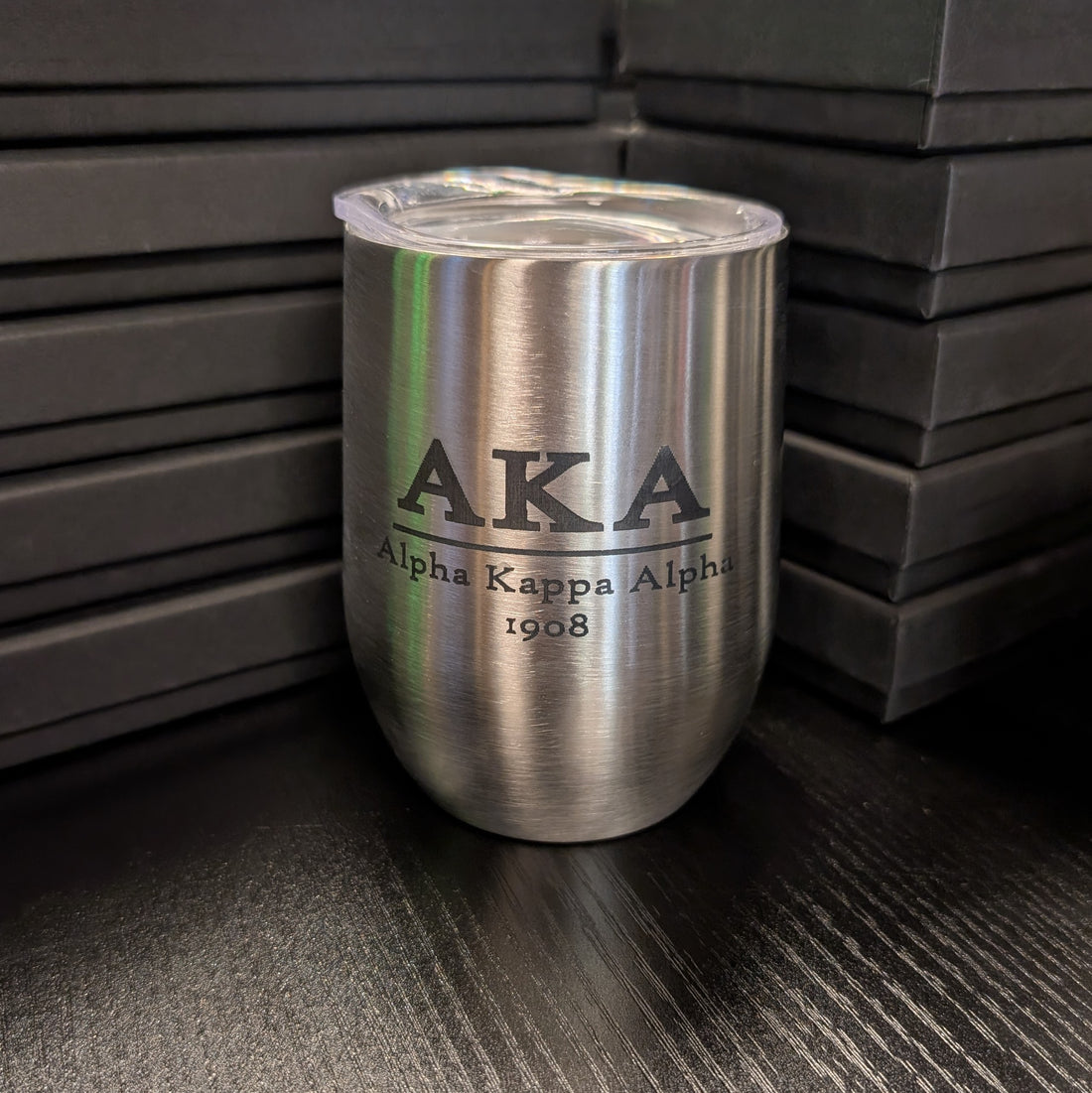 Silver tumbler with 'AKA Alpha Kappa Alpha 1908' engraving on a dark surface.