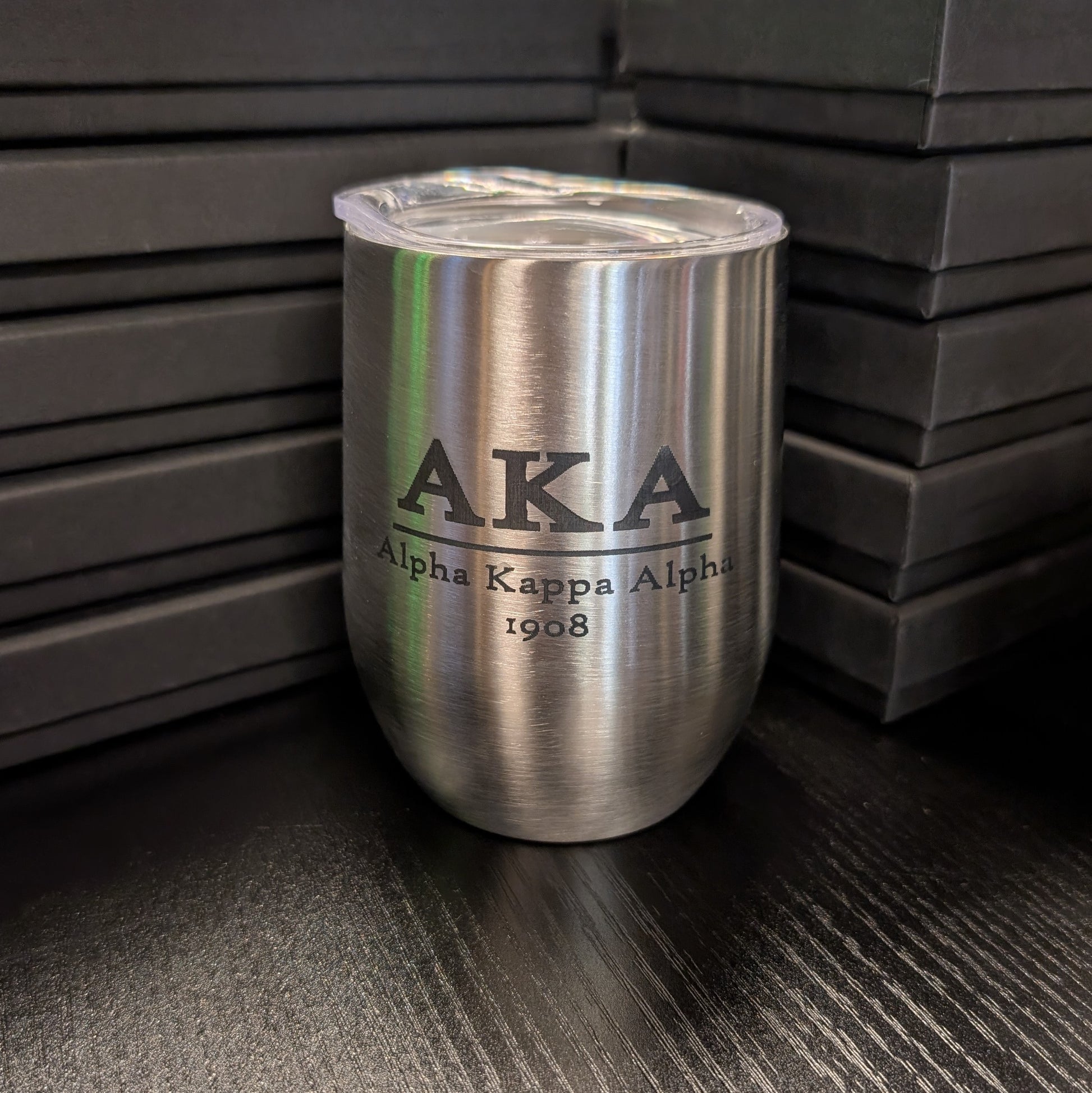 Silver tumbler with 'AKA Alpha Kappa Alpha 1908' engraving on a dark surface.