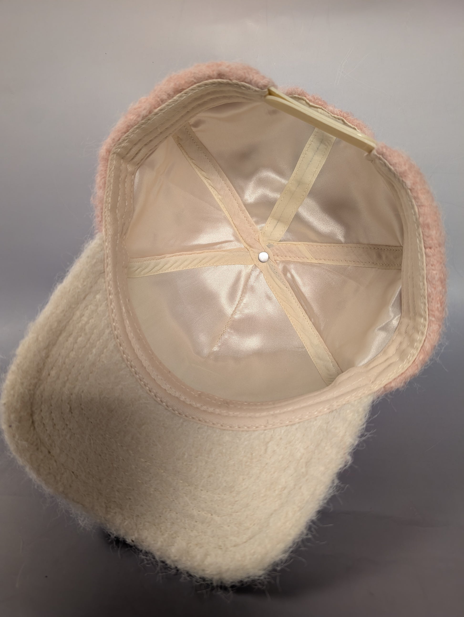 cream satin lined underside of a pink fur hat with a cream bill