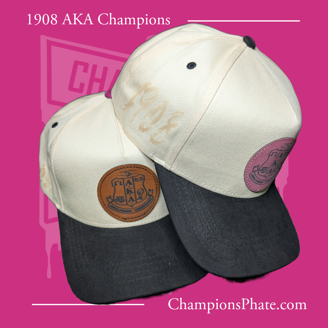 Two AKA fraternity caps with pins, one featuring a suede brim and the other with a leather patch, displayed against a pink background.