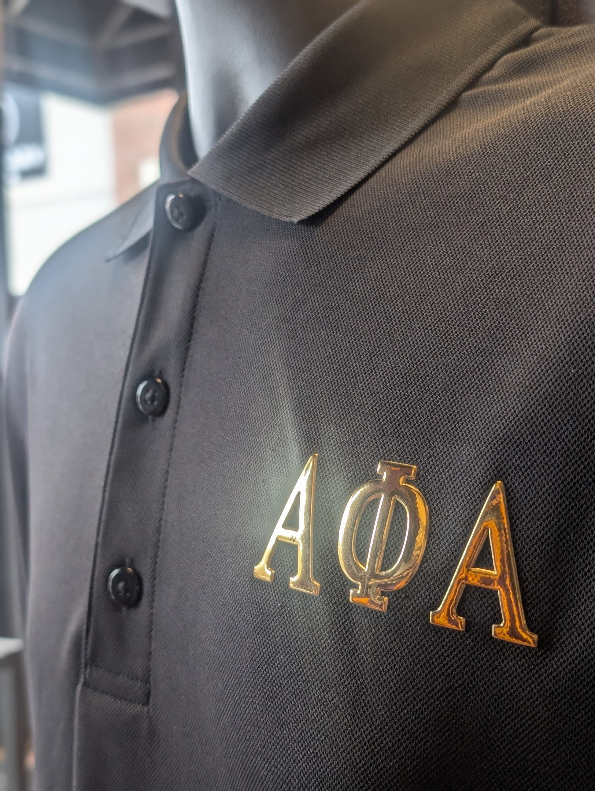 Black polo shirt with gold greek letters for alpha on the left chest