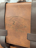 Close-up of a brown faux-leather bag with dark brown straps and the logo for zeta amicae engraved in it