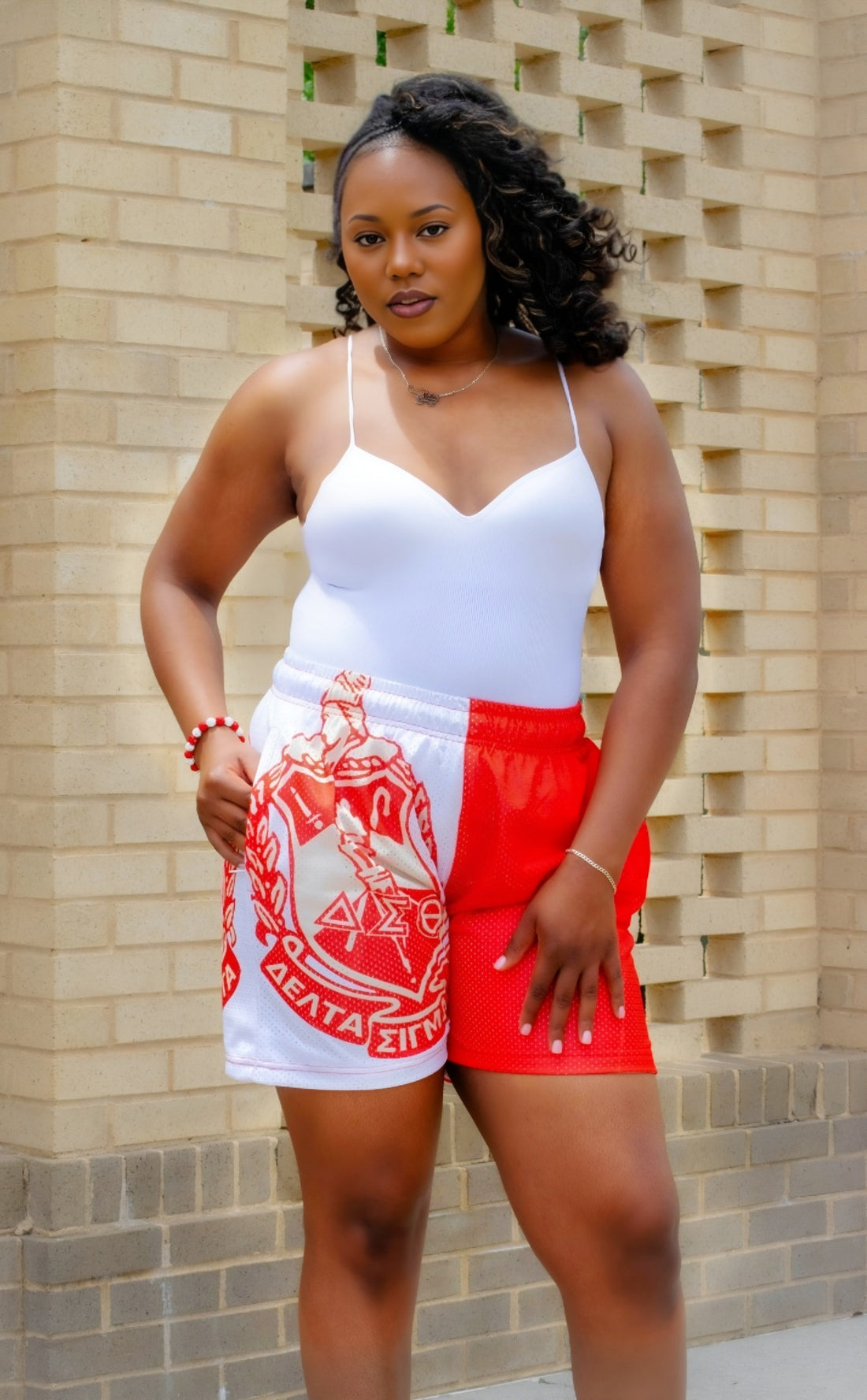Woman wearing a white top and red shorts with a graphic design, standing against a brick wall.