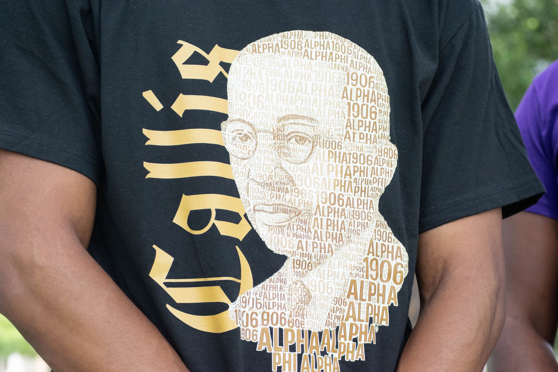 Person wearing a black t-shirt with a graphic design of a face made from text and the word 'Alpha'.