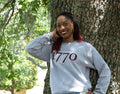 Person wearing a gray sweatshirt with '1770' printed on it, leaning against a tree outdoors.