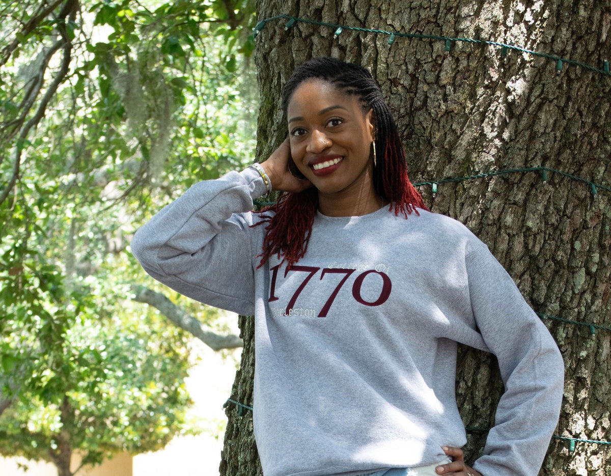 Person wearing a gray sweatshirt with '1770' printed on it, leaning against a tree outdoors.