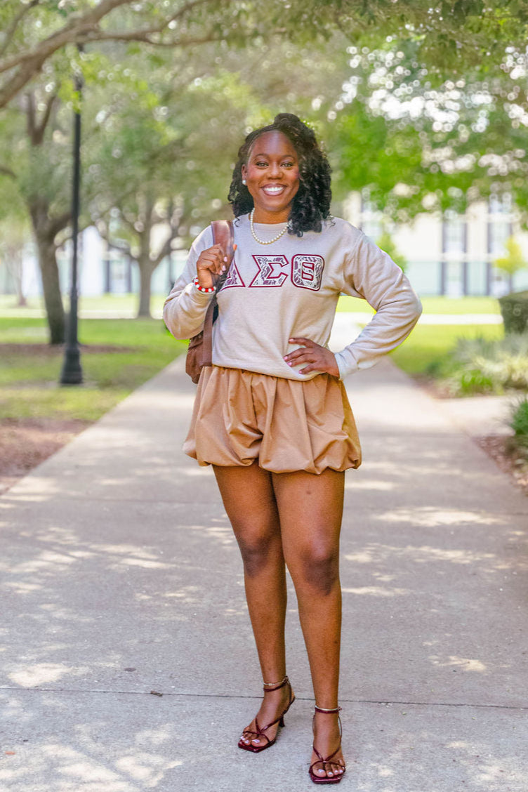 Woman wearing a sweatshirt with a logo and shorts, standing on a path outdoors.