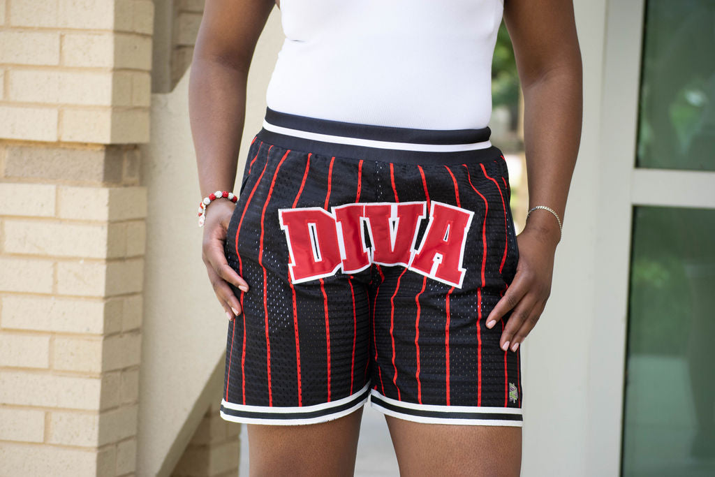 Person wearing black shorts with red pinstripes and 'DIVA' text, standing outdoors.
