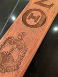 A collection of wooden paddles with various Greek letters and emblems engraved on them, displayed side by side.
