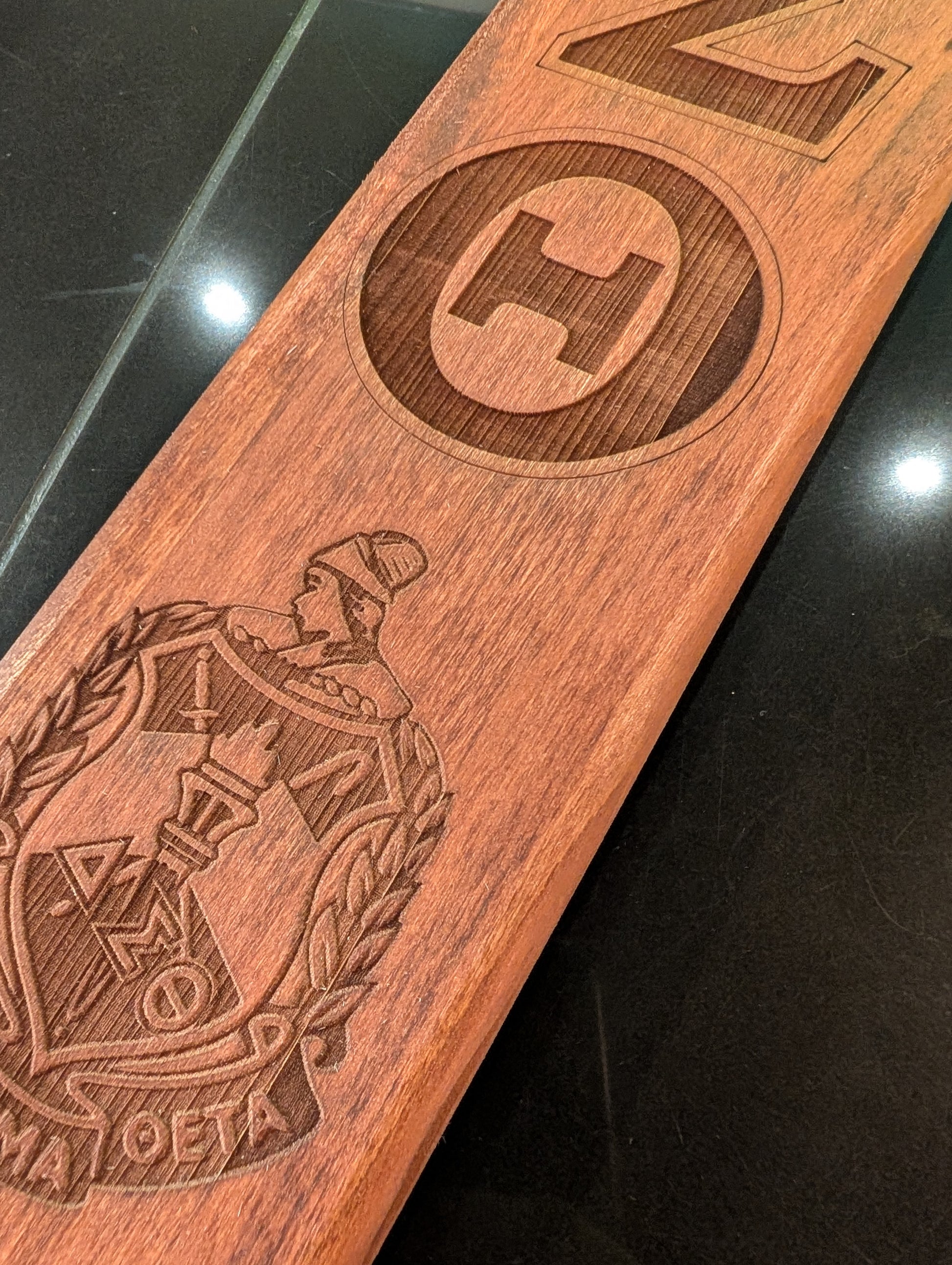 A collection of wooden paddles with various Greek letters and emblems engraved on them, displayed side by side.