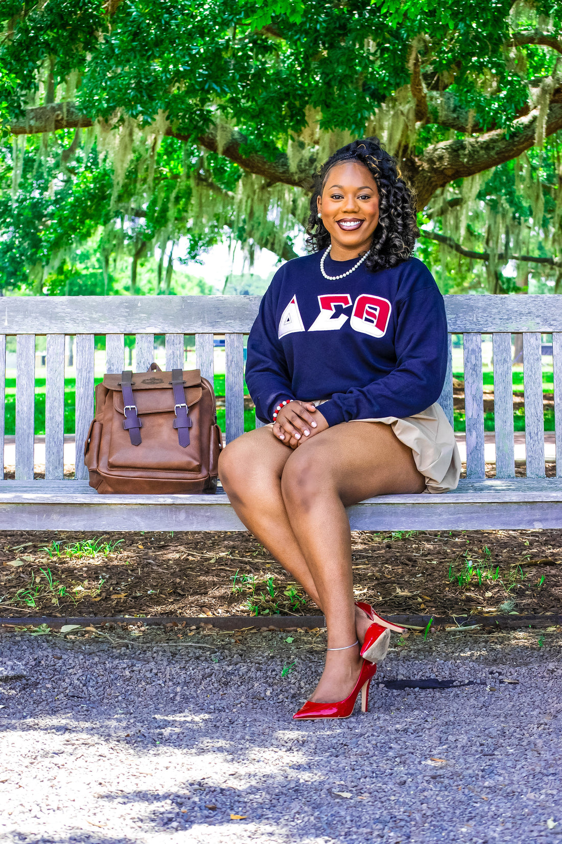 Woman sitting on a bench outdoors with a backpack next to her, wearing a black sweatshirt with a logo.
