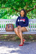 Woman sitting on a bench outdoors with a backpack next to her, wearing a black sweatshirt with a logo.