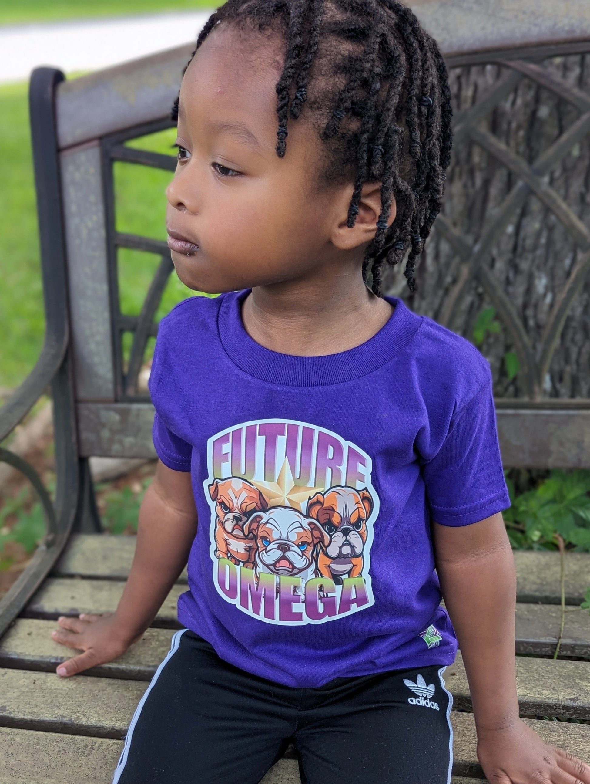 Child wearing a purple t-shirt with 'Future Omega' and bulldog graphics, sitting on a wooden bench.