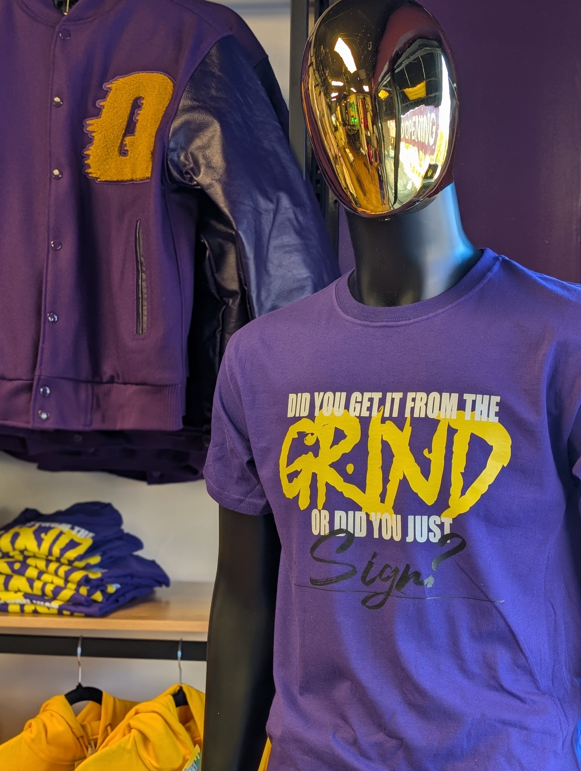 Mannequin wearing a purple t-shirt with yellow text, surrounded by purple and yellow clothing items.