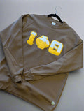 Brown sweatshirt with yellow and white graphic design on a plain background