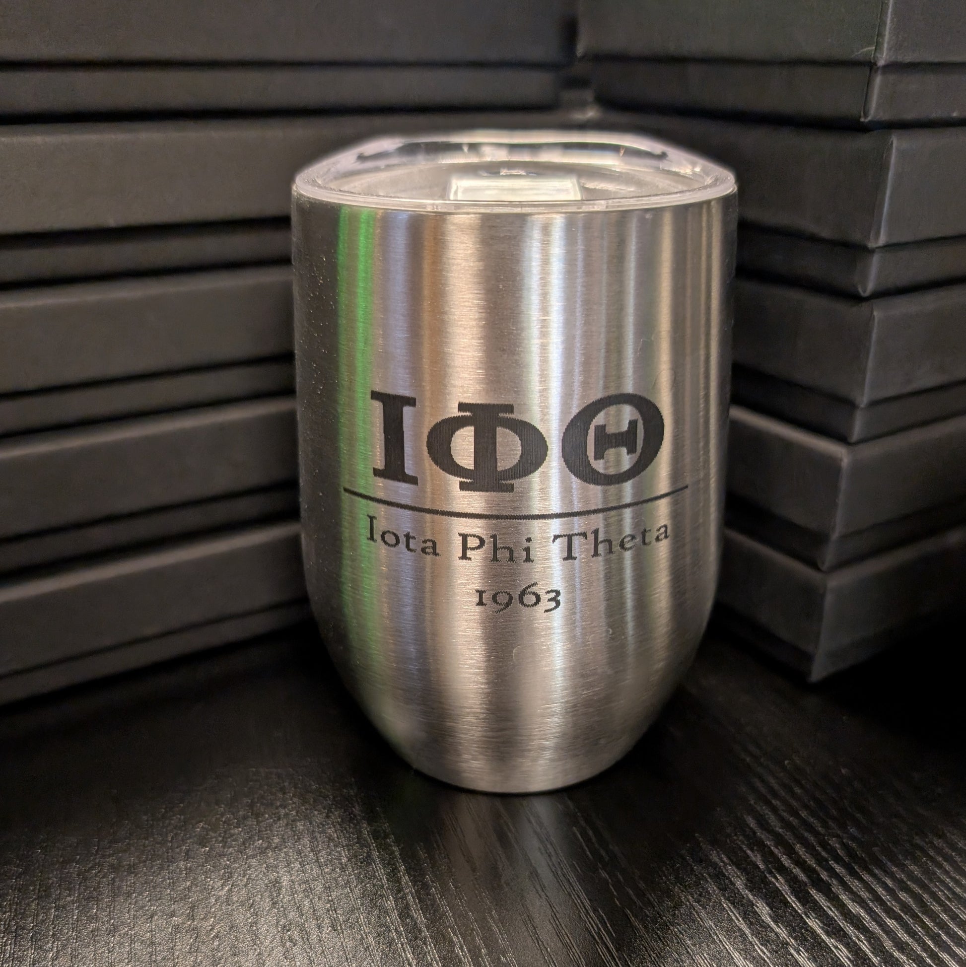 Silver tumbler with Iota Phi Theta logo on a dark surface