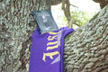 Purple t-shirt with yellow text draped over a tree branch
