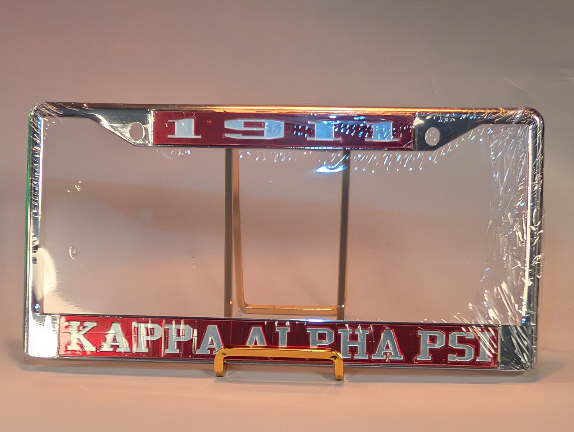 Kappa Alpha Psi license plate frame on a stand with clear plastic wrap.