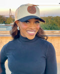 Woman wearing a beige cap with a logo, standing outdoors with a blurred background