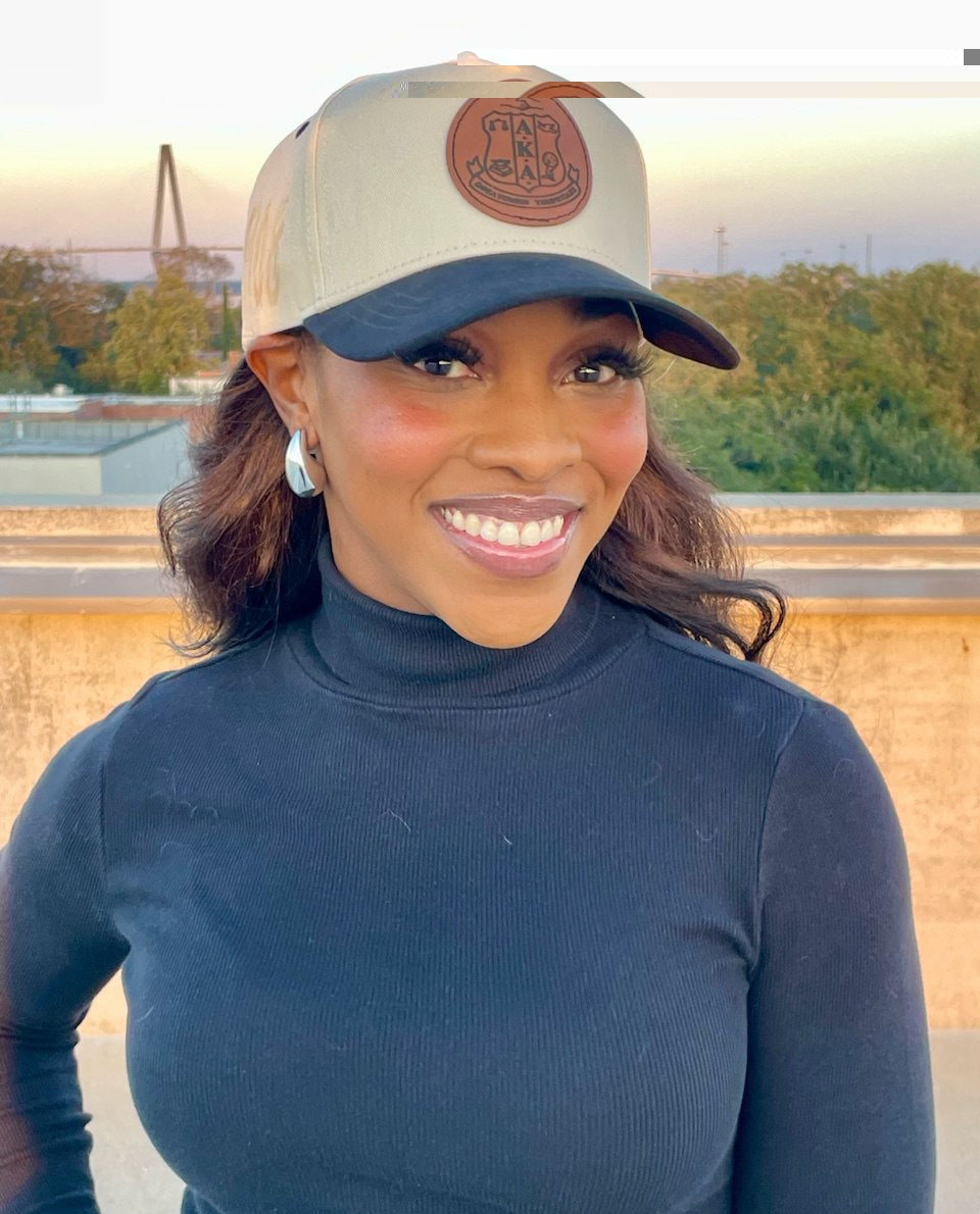 Woman wearing a beige cap with a logo, standing outdoors with a blurred background