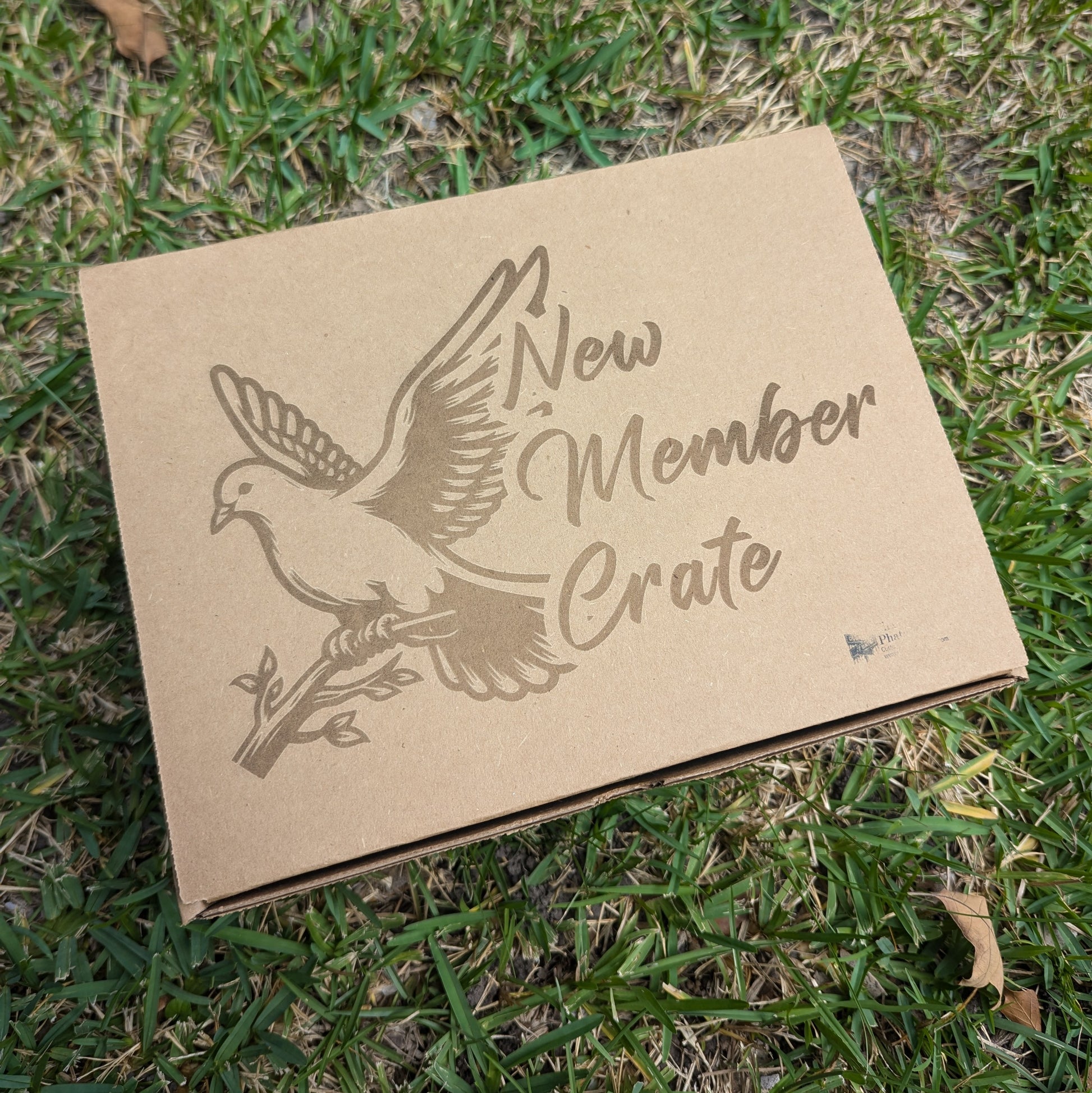 A cardboard gift box with 'NEW MEMBER CRATE' printed on it, featuring an embossed design of a dove perched on a branch 