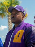 Person wearing a purple cap and omega psi phi varsity jacket with a yellow chenille 'Q' 