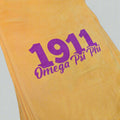 Yellow towel with purple '1911 Omega Psi Phi' text on a black background