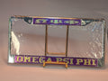 Omega Psi Phi license plate frame on a stand with clear plastic wrap.