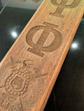 A collection of wooden paddles with various Greek letters and emblems engraved on them, displayed side by side.