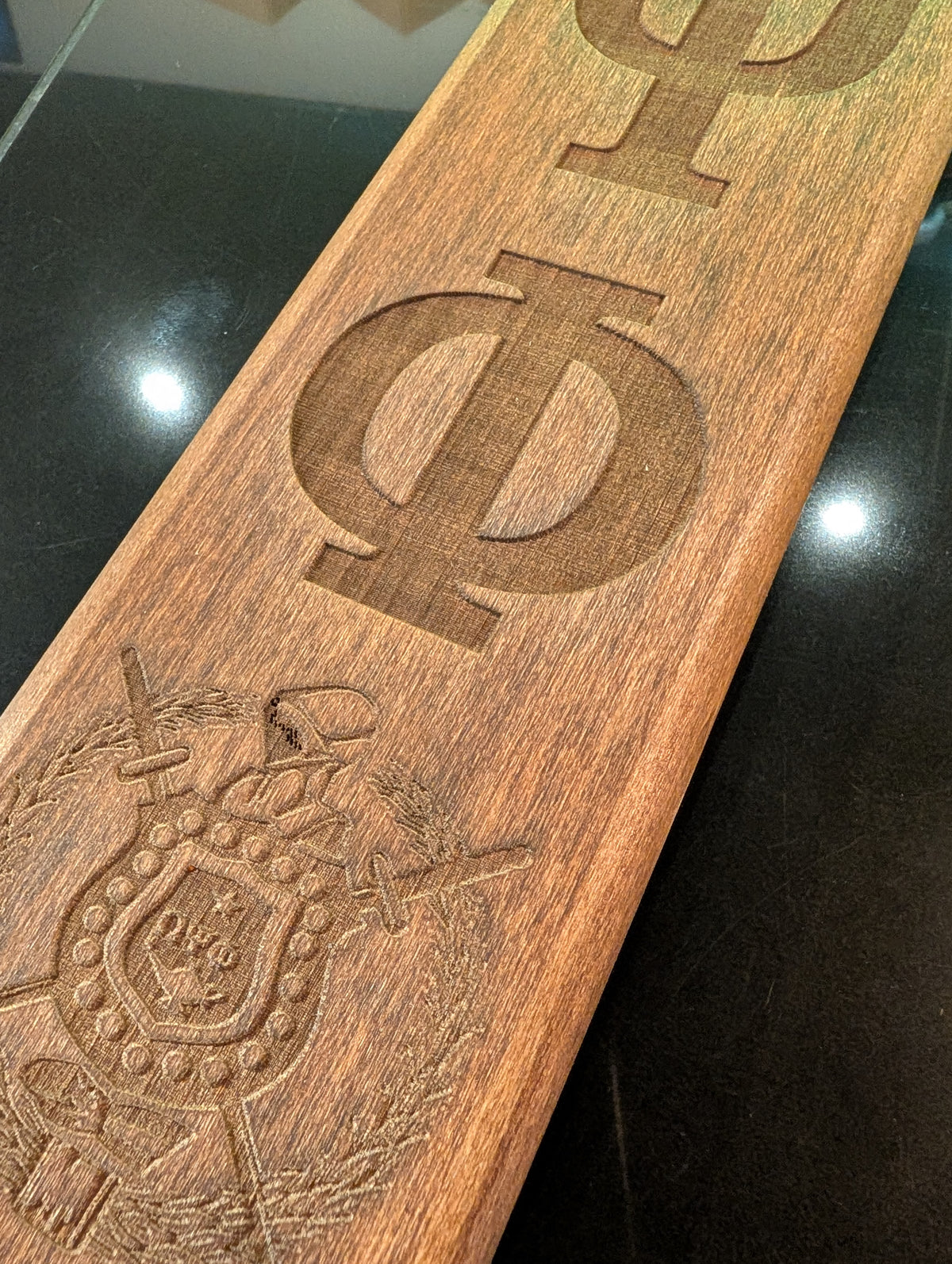 A collection of wooden paddles with various Greek letters and emblems engraved on them, displayed side by side.