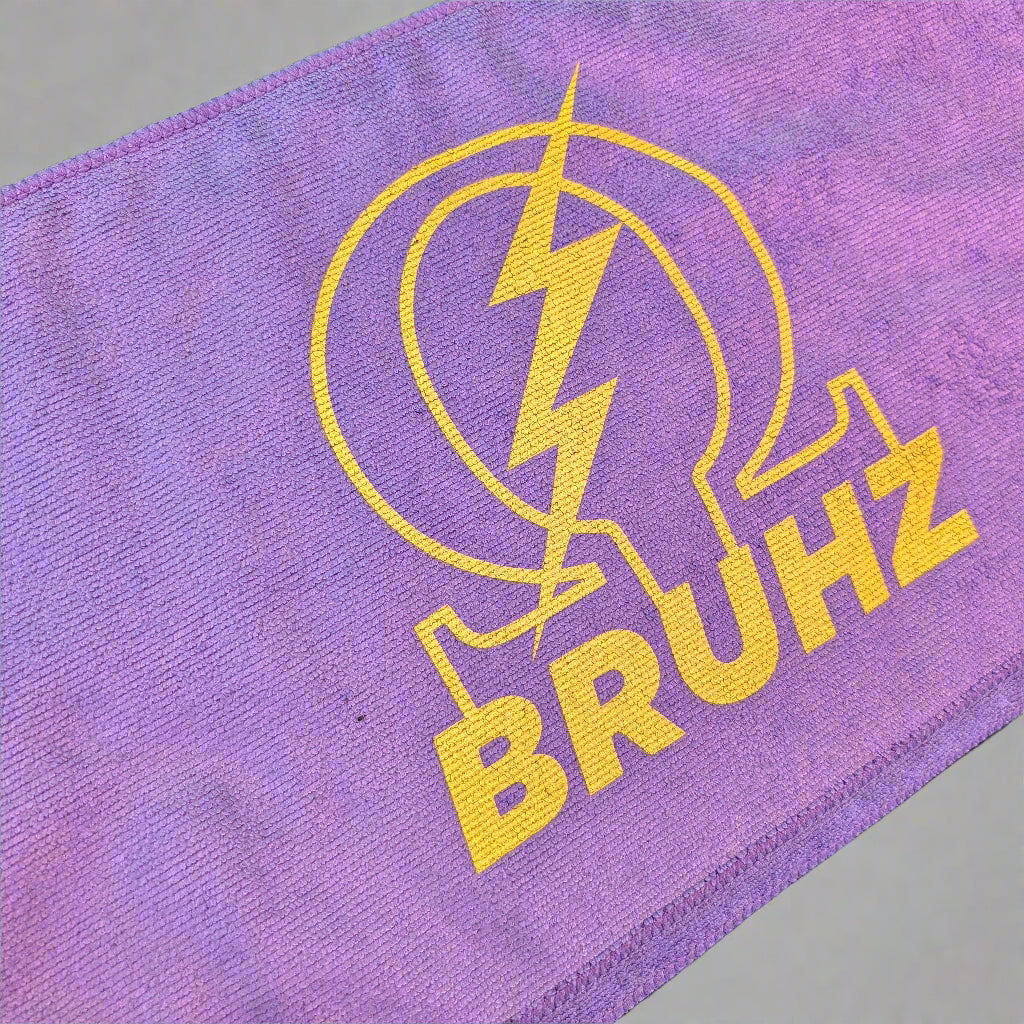 Purple towel with yellow 'BRUHZ' logo on a dark surface