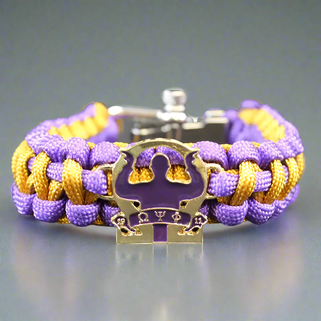 Purple and gold braided bracelet with a central emblem 