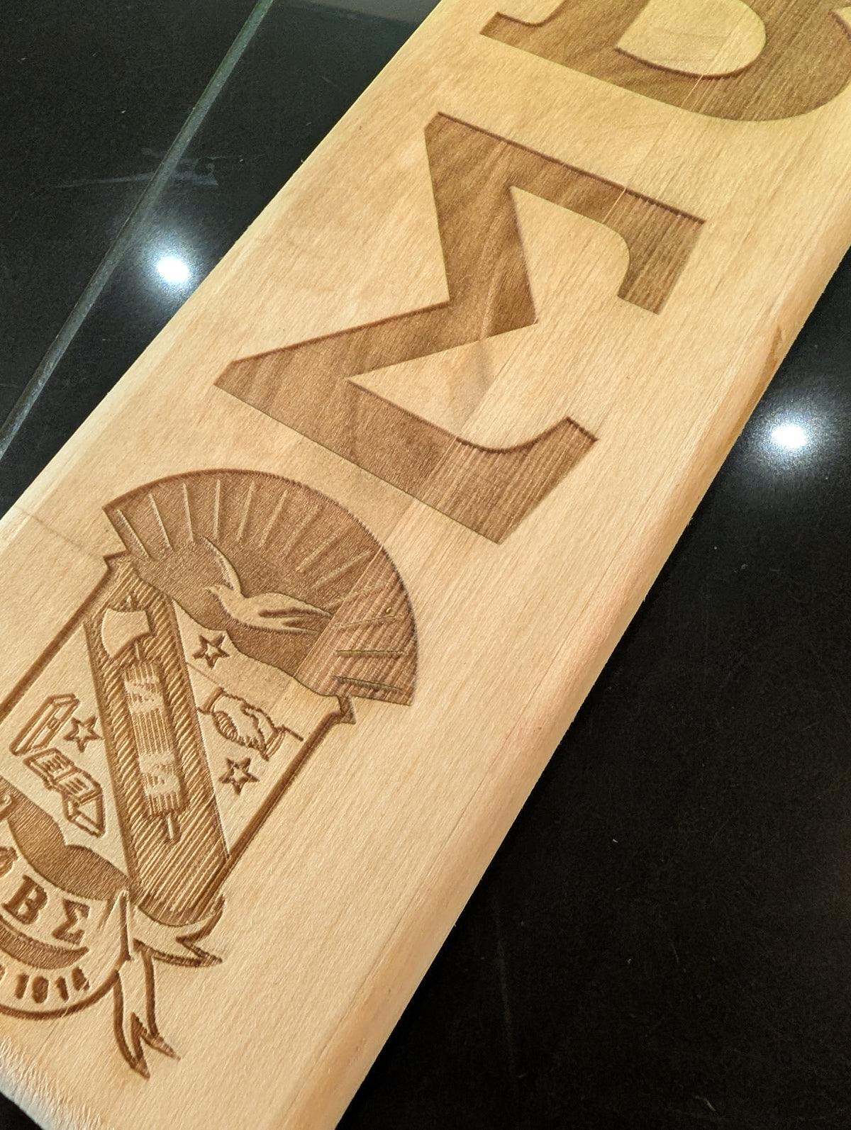 A collection of wooden paddles with various Greek letters and emblems engraved on them, displayed side by side.