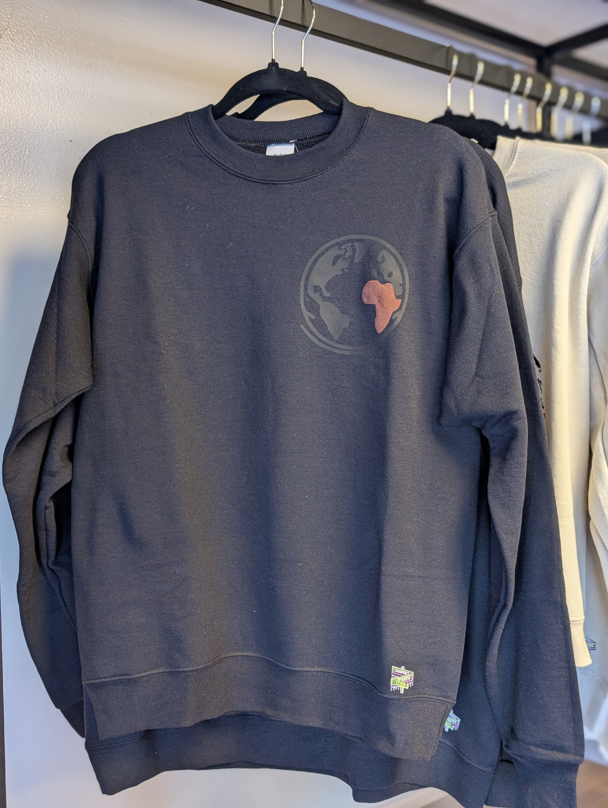 black sweatshirt with a world map design on a hanger against a white wall.