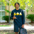 Person wearing a black sweatshirt with gold letters, holding a backpack outdoors.