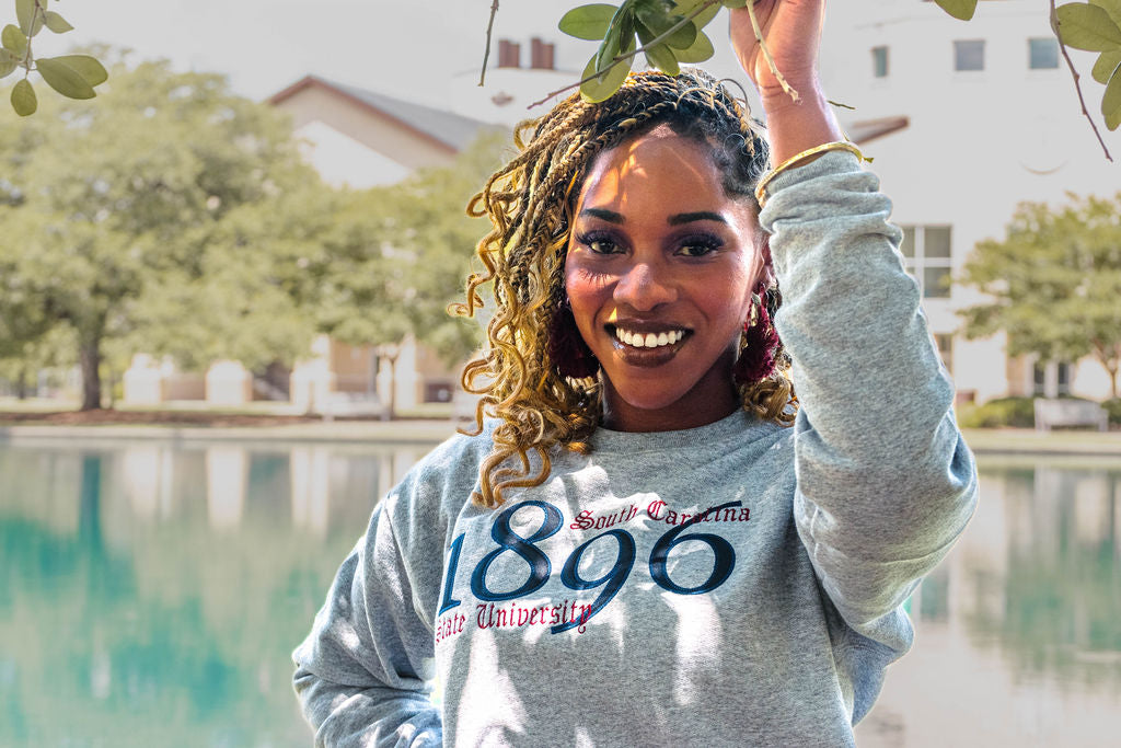 Person wearing a gray sweatshirt with '1896' and 'South Carolina' text, holding leaves by a pool.