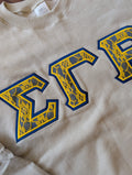 Close-up of a beige crewneck sweatshirt with blue and yellow Greek letters 'SGR' embroidered on the front.