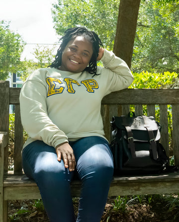 Person wearing a light green sweatshirt with 'Sigma Gamma Rho' letters, sitting on a wooden bench outdoors.