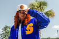 Person wearing a blue jacket with a yellow logo and a white cap outdoors