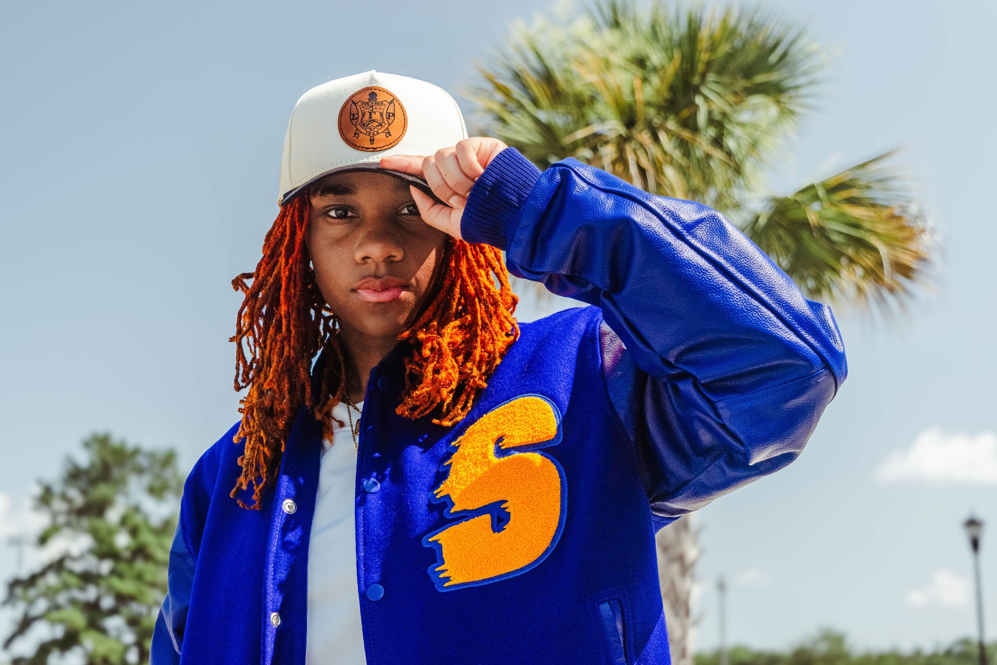 Person wearing a blue jacket with a yellow logo and a white cap outdoors